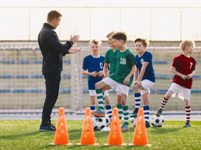 gettyimages-1293633657-170667a Group of young boys on football training. Kids practicing soccer on grass field. Young man as a soccer coach explaing to players training rules. Children exercising with soccer balls